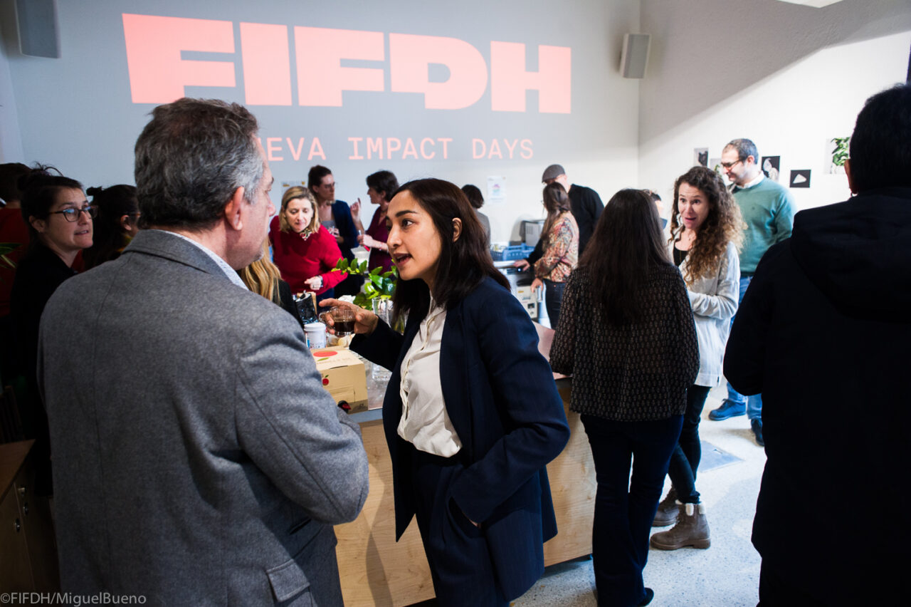 Des gens discutent de manière informelle devant un mur sur lequel est projeté l'inscription "FIFDH Geneva Impact Days"