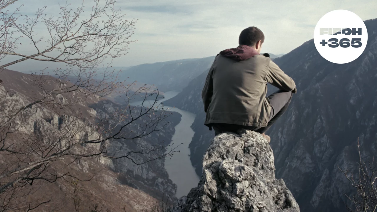 Un homme assis au sommet d'une montagne, contemplant une rivière en contrebas.